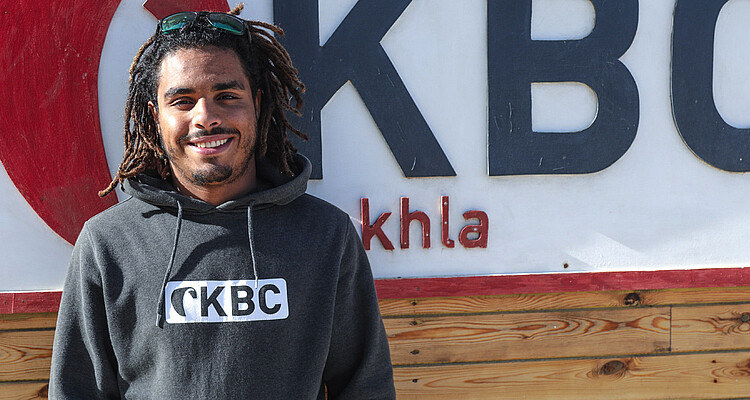 Aufstieg kitesurfer met dreadlocks bij kiteboard club, draagt CKBC hoodie en zonnebril bij watersport centrum