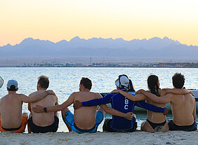 Kitesurfers groep omhelzend op strand bij zonsondergang met bergen - KBC Kitesurf Center Ras Soma downwind trip