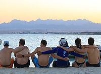 Kitesurfers groep omhelzend op strand bij zonsondergang met bergen - KBC Kitesurf Center Ras Soma downwind trip
