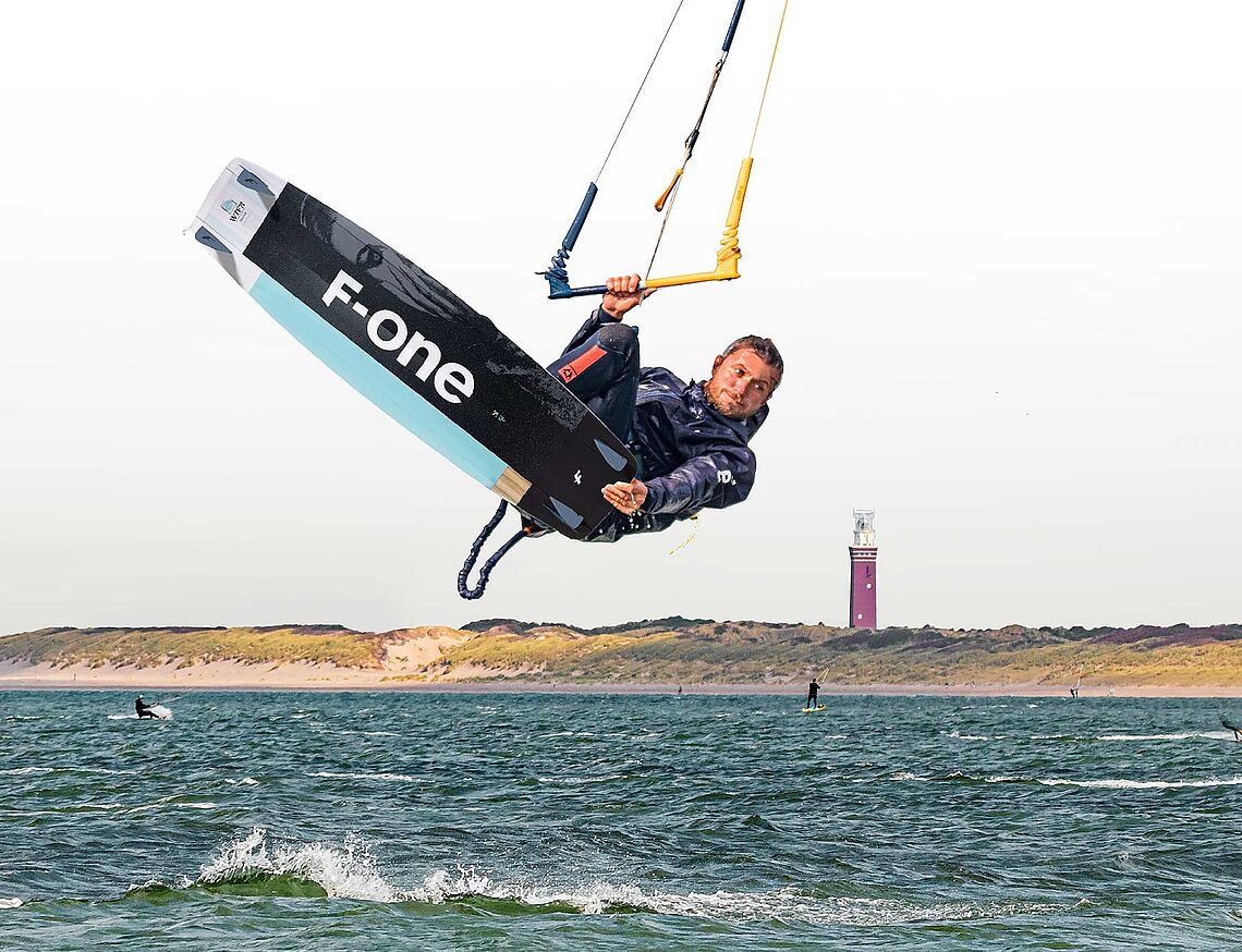 KBC Brouwersdam kitesurfer jumps spectacularly over water with F-One board, lighthouse in the background, kite spot Holland