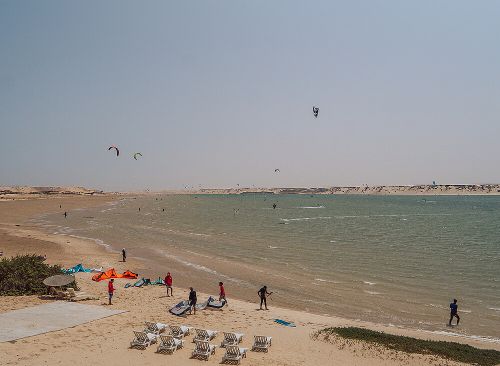 Kiteboarding beach Dakhla with NewSpiritDakhla - kitesurfers on water, colorful kites in sky, sand dunes backdrop