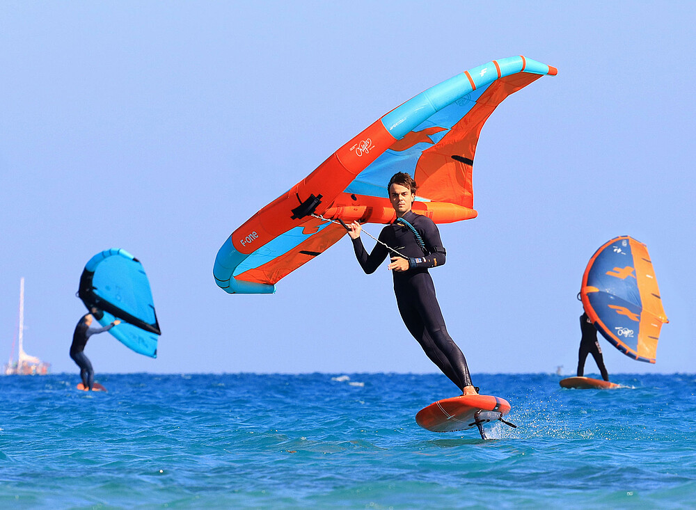 Wingfoil Event - Kitesurfer op hydrofoil met wing boven blauw water, watersport actie op strand