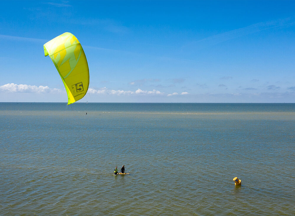 Kitesurfen in Holland: Gelber Kite über ruhigem Wasser, Kitesurfer auf dem Board - perfekte Bedingungen für Wassersport