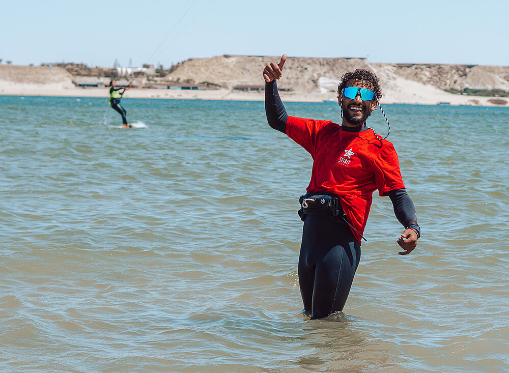 NewSpiritDakhla Kitesurf instructor giving thumbs up at Dakhla beach with kitesurfer in background