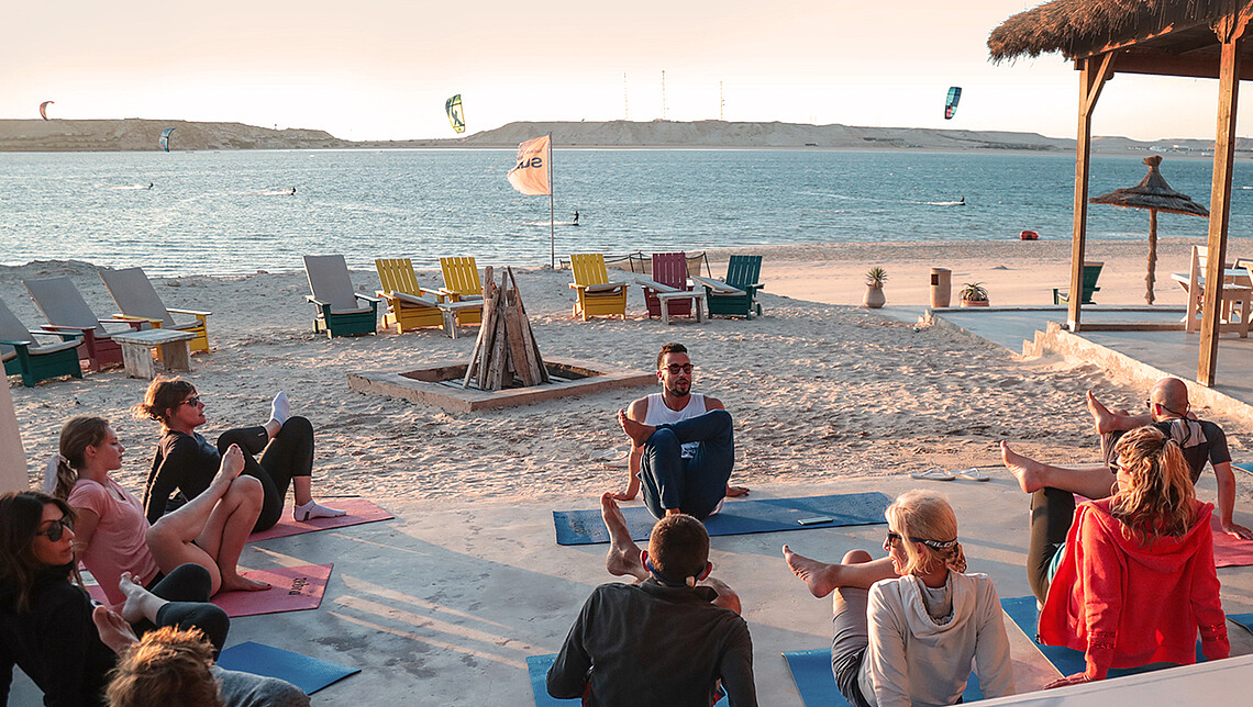 YogaundKitesurfen strand yoga sessie bij zonsondergang met kitesurfen op achtergrond - wellness en watersport