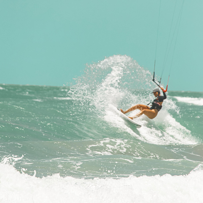 BR Girls Event Kitesurf Yoga: Kitesurfista saltando sobre ondas turquesa durante kitesurf na praia tropical
