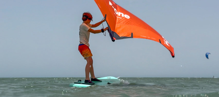 Wingfoilcursus voor kinderen bij KBC Dakhla - Jonge wingfoiler op het water met oranje vleugel in Dakhla Marokko