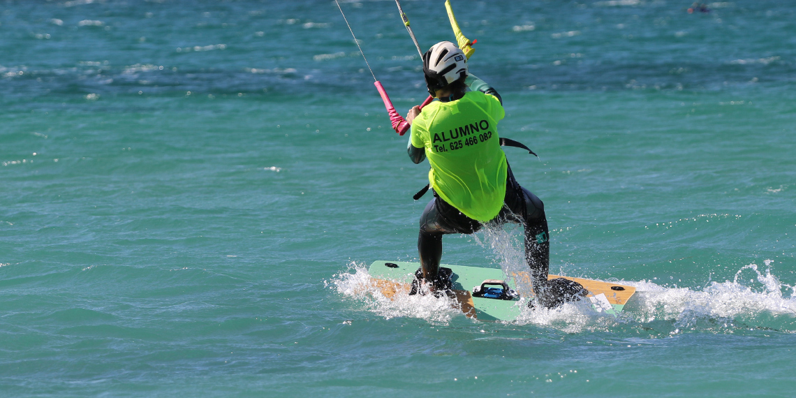 Kitesurfer in green Alumno shirt kiteboarding on turquoise water - water sports travel destination beach activity