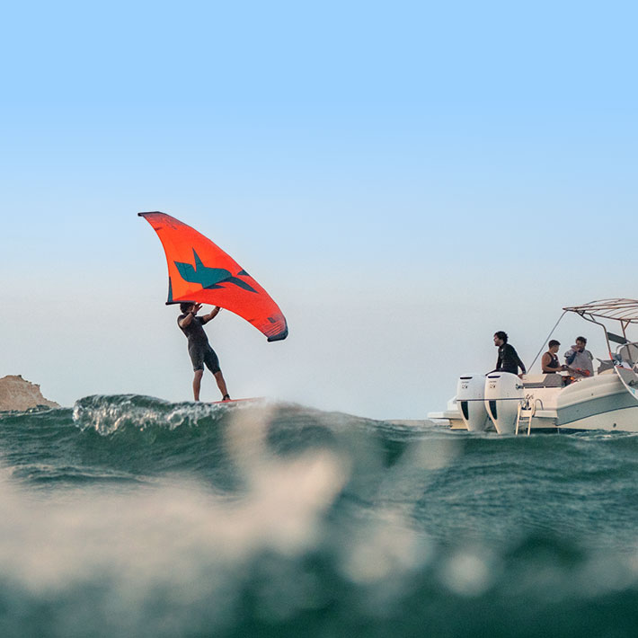 Kitesurfer riding wave with red kite, boat nearby - Lagoon Trip White Dune at KBC New Spirit Kitesurf Center Dakhla Morocco