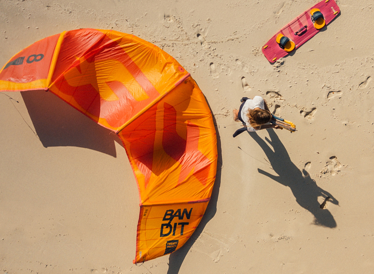 Kitesurf Lexikon: Orange Bandit Kite am Sandstrand mit Kitesurfer - Kiteboarding Ausrüstung und Wassersport