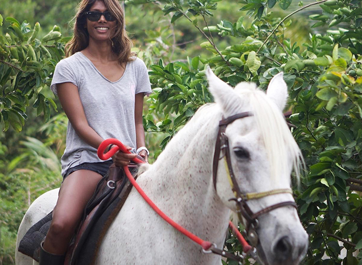 Parajuru Activities: Woman horseback riding white horse through tropical vegetation at kiteboarding travel destination