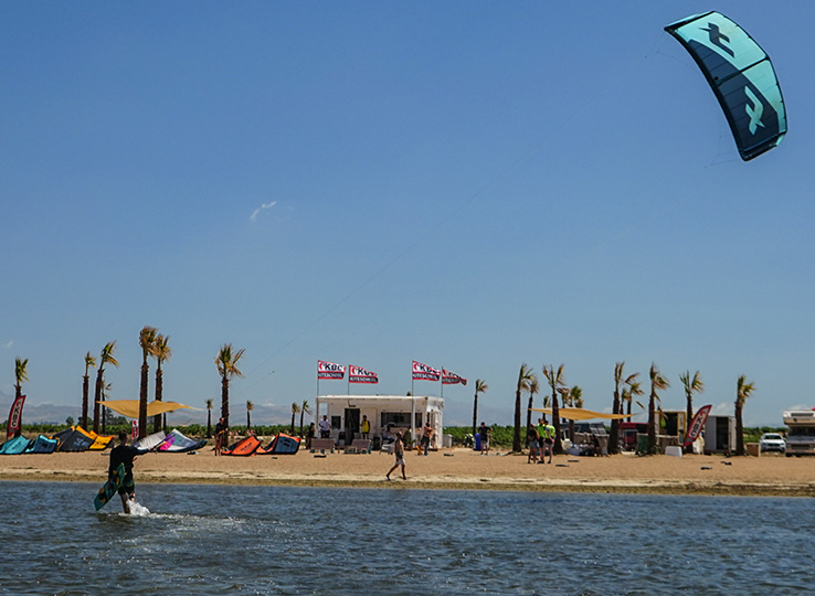 Sizilien Kiteurlaub: Kitesurfer on beach with turquoise kite, palm trees and kite school - perfect kiteboarding destination