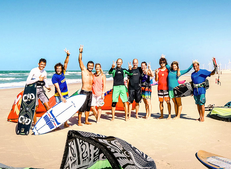 Happy kiteboarding group on beach with kites and boards - kitesurfing travel destination and water sports vacation
