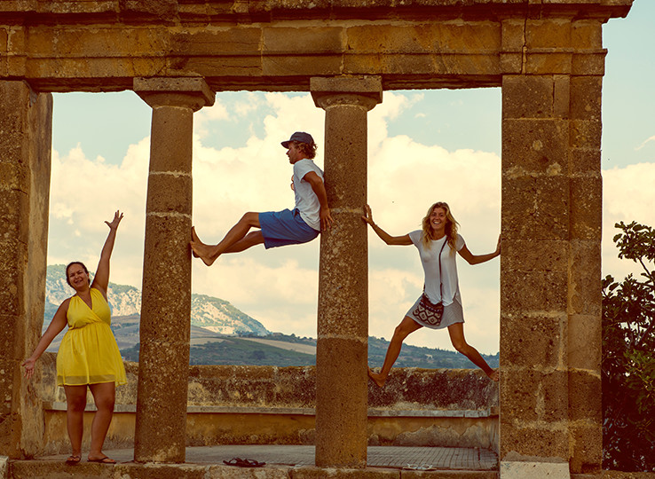 Three travelers jumping at ancient ruins with mountain views - perfect backdrop for kitesurfing adventures