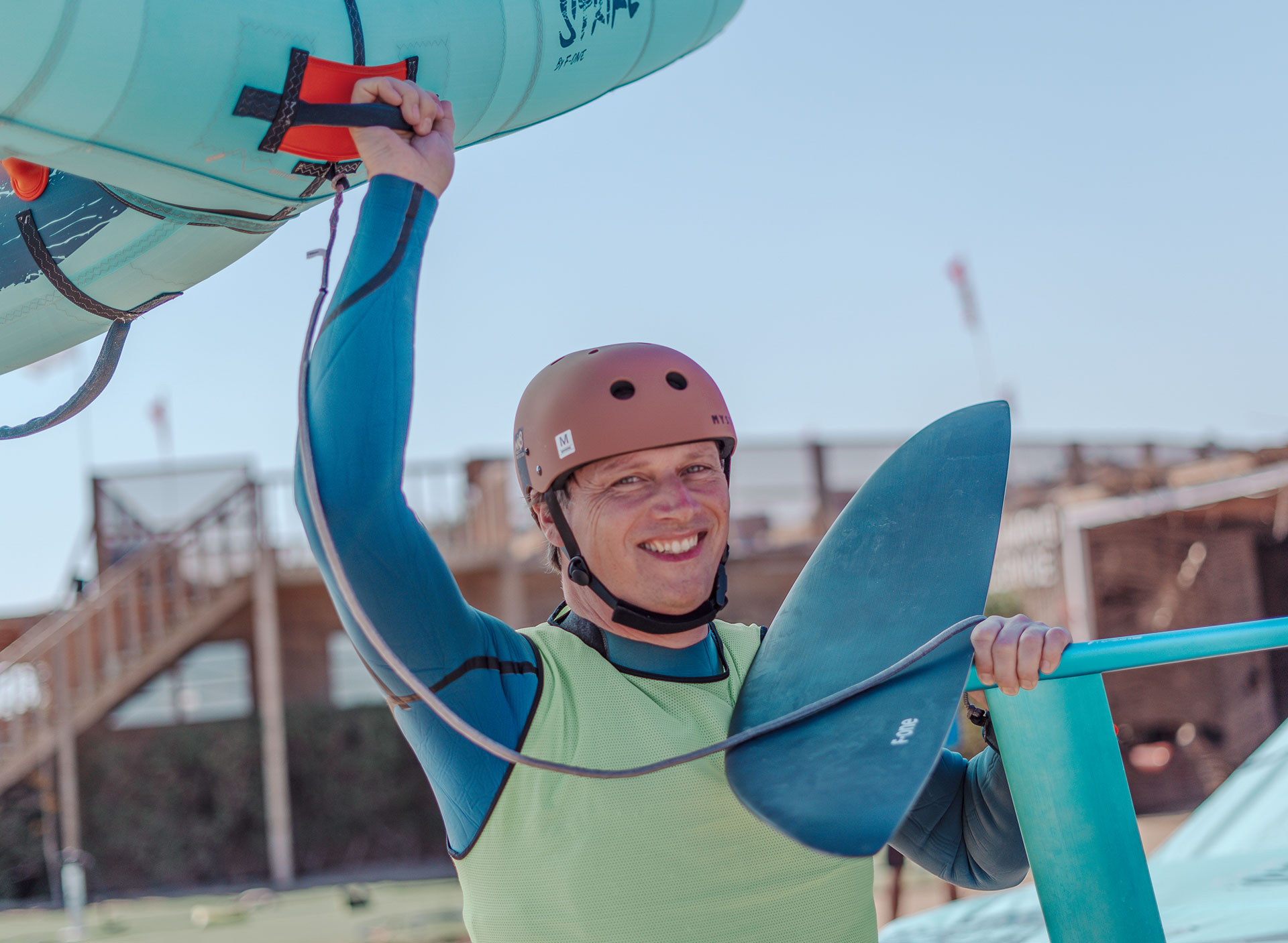 Wingfoil Event: Glimlachende kitesurfer met helm draagt wingfoil-uitrusting op strand, watersport bestemming